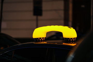 Taxi car with yellow checkered sign on city street in evening, closeup