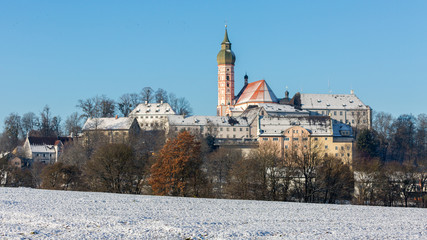 ANDECHS, BAVARIA / GERMANY - December 3, 2019: Panorama (16:9) of Kloster Andechs during winter. A snow covered field and trees in the foreground. Benedictine monastery / abbey, baroque architecture.