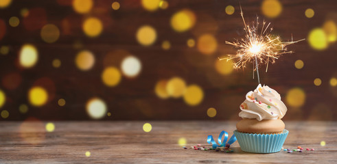 Birthday cupcake with sparkler on wooden table, space for text. Bokeh effect