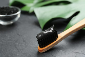 Bamboo toothbrush with charcoal paste on black stone table, closeup. Space for text