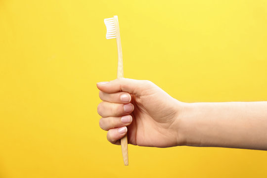 Woman holding bamboo toothbrush on yellow background, closeup