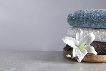 Stack of clean bath towels and beautiful flower  on grey table. Space for text