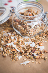 Top view of a glass jar up to the top filled with organic granola with nuts and coconut. Jar with granola on a background of baking paper. Healthy lifestyle concept.