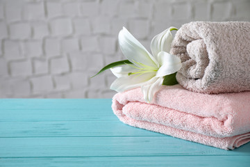 Folded clean soft bath towels and beautiful flower on blue wooden table. Space for text