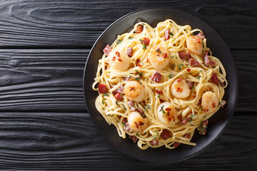 Spicy spaghetti served with scallops and bacon in cream cheese sauce close-up in a plate. Horizontal top view