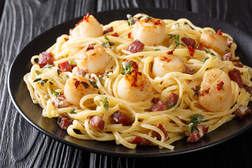 Mediterranean pasta with fried scallops, bacon in a creamy cheese sauce with herbs close-up in a plate. horizontal
