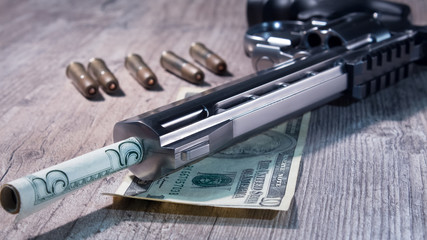 Naklejka premium A pistol with bullets and money dollars lies on wooden the table. Revolver close-up.