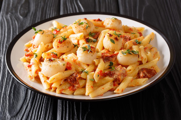 Hot penne pasta with fried scallops, tomatoes, cheese and thyme close-up in a plate. horizontal