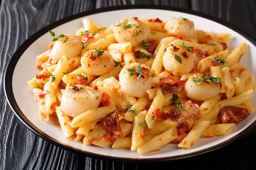 Mediterranean pasta with fried scallops, dried tomatoes and thyme close-up in a plate. horizontal