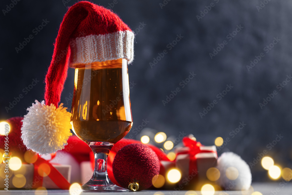 Wall mural Festive glass of light beer on the table with Christmas gifts and garland dark background