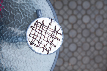 A cup of coffee with cream stands on a glass table