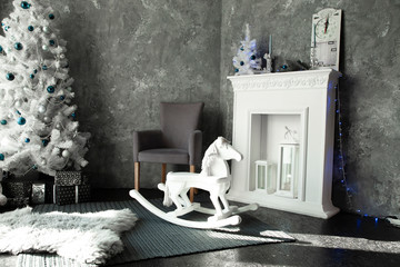 Room with a gray wall, a white fireplace and a silver Christmas tree
