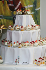 Mini cakes decorated with whipped cream and fresh red currant. Sweet tasty snacks at the party. Food photography. Lots of pastry pieces on the plate. Catering service