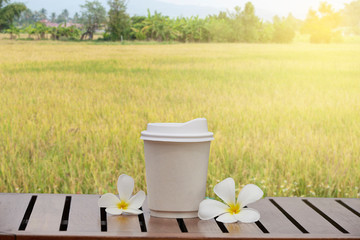 Paper coffee cup or disposable coffee cup above wood table on yellow field background.