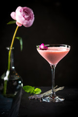 pink alcoholic cocktail decorated with roses and mint close-up on black background with copy space. pink drink for bar menu