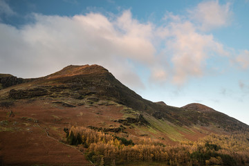 Fototapeta na wymiar Majestic vibrant Autumn Fall landscape Buttermere in Lake District with beautiful early morning sunlight playing across the hills and mountains