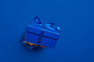 close-up of female hand holding a present gift box through a torn dark blue paper, mockup. Copy space for text