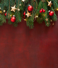 Christmas border with fir branches, red baubles and gold stars on the wooden board painted in dark-red with copy space for text. Flat lay. Christmas and New Year holidays background.