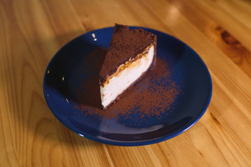 Snickers cheesecake on a blue saucer on a large bright wooden table