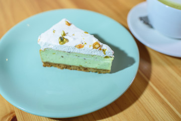 Matcha latte and pistachio cheesecake on a large bright wooden table