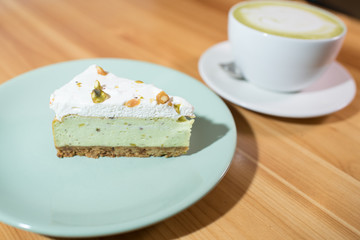 Matcha latte and pistachio cheesecake on a large bright wooden table