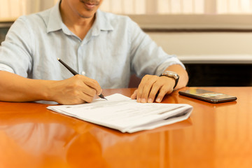 Businessman signing documents with quill pen on wooden desk at home.