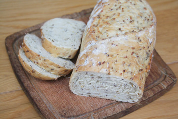 Partially sliced wholegrain organic bread with different seeds on a wooden cutting board on table