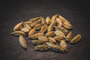 Close up view of cardamom seeds in black slate background. 