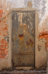 Closeup neglected vintage rusty steel door with wooden doorframe on brick wall with cement plaster 