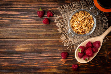 Granola in glass jar and raspberry on dark wooden background.