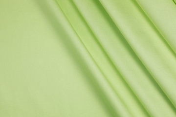 The green satin fabric  is laid out on the table. Soft folds of material drapery have pronounced diagonal direction. Copy space