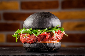 American food concept. Black bun burger with the words meat and burger, with veal tartar, tomato...