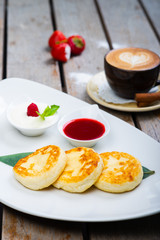 Traditional breakfast with coffee and cheesecakes, cottage cheese pancakes on a plate with syrup and jam.