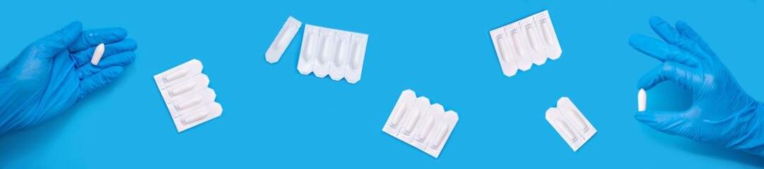 White suppositories for anal or vaginal use in the doctor's gloved hand on a blue background. Medical candles for treatment of Candida, thrush, hemorrhoids, inflammation and fever. extra wide banner