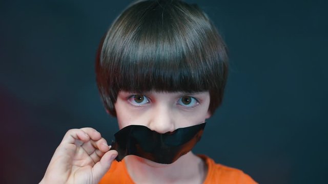 The boy peels off adhesive tape from his mouth.