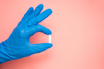 White suppository for anal or vaginal use in hand of a doctor wearing gloves on a pink background....