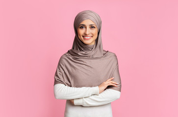 Portrait of happy arab girl in hijab over pink studio background
