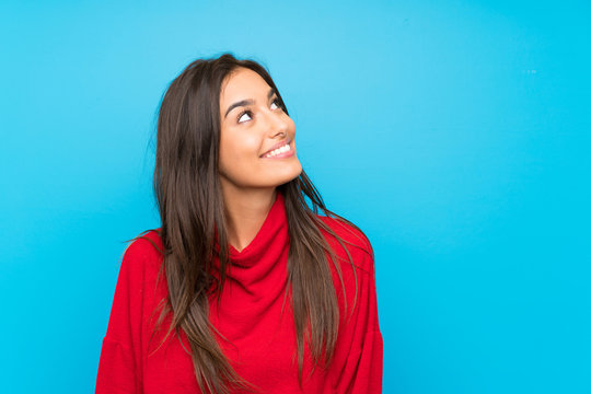 Young woman with red sweater over isolated blue background laughing and looking up