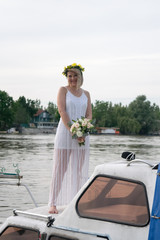 beautiful bride with wedding bouquet standing on a boat and posing for the photographer near the river