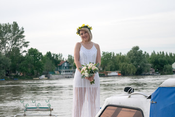 beautiful bride with wedding bouquet standing on a boat and posing for the photographer near the river