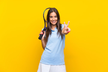 Young tennis player woman over isolated yellow wall smiling and showing victory sign
