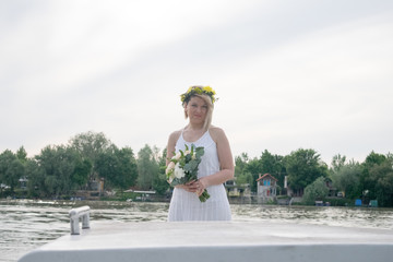 beautiful bride with wedding bouquet standing on a boat and posing for the photographer near the river