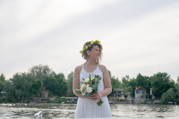 beautiful bride with wedding bouquet standing on a boat and posing for the photographer near the river