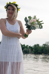 beautiful bride with wedding bouquet standing on a boat and posing for the photographer near the river