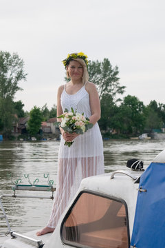 beautiful bride with wedding bouquet standing on a boat and posing for the photographer near the river