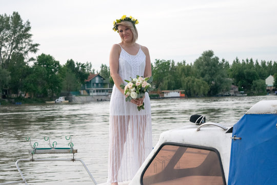 beautiful bride with wedding bouquet standing on a boat and posing for the photographer near the river