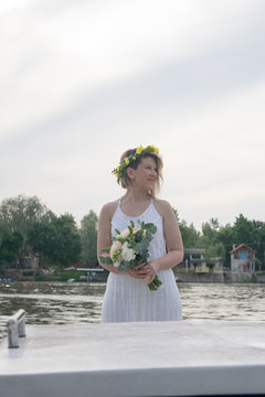 beautiful bride with wedding bouquet standing on a boat and posing for the photographer near the river