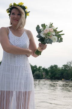 beautiful bride with wedding bouquet standing on a boat and posing for the photographer near the river