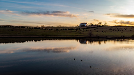 Sunset over rural countryside pond reflecting trees and clouds as ducks and geese swim