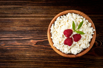 Cottage cheese with raspberry in wooden bowl on dark wooden background.